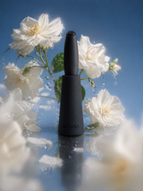Black NŌARA handheld frother in silicone stand surrounded by white flowers