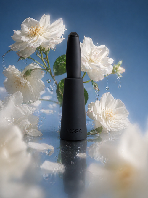 Black NŌARA handheld frother in silicone stand surrounded by white flowers