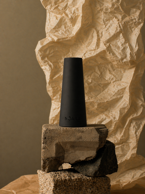 Black NŌARA silicone frother stand displayed on stacked stone blocks