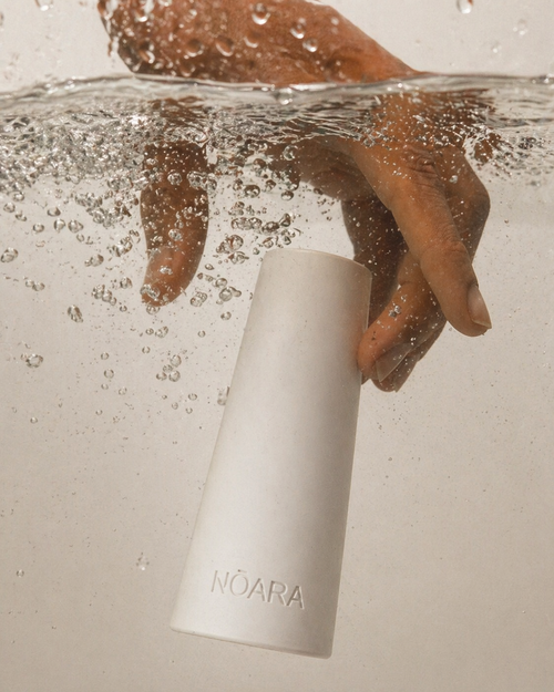 White NŌARA silicone frother stand submerged in water with hand and water droplets