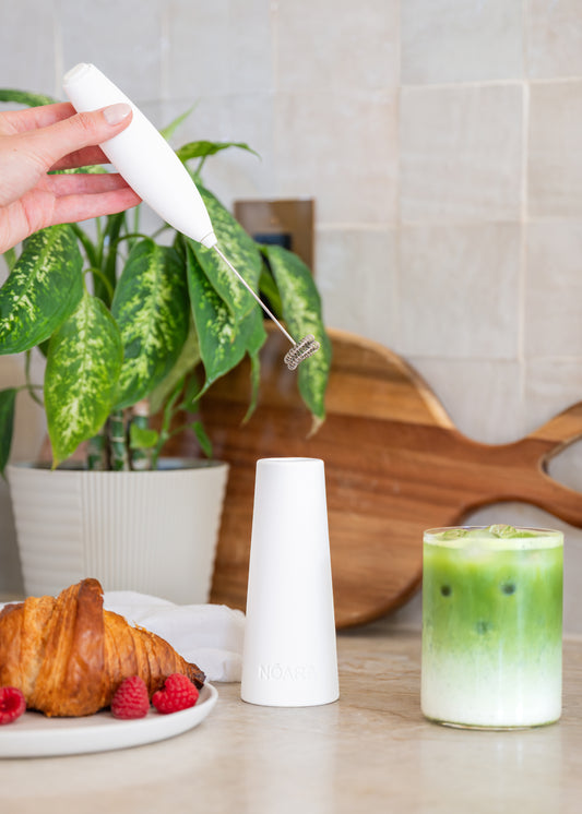 White NŌARA handheld frother and silicone stand for making iced matcha lattes at home.